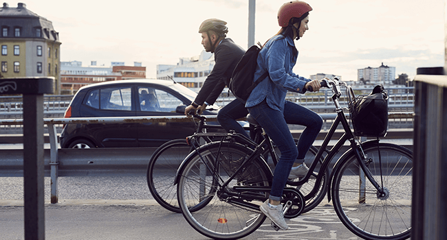 Man och kvinna cyklar längs bilväg i stadsmiljö