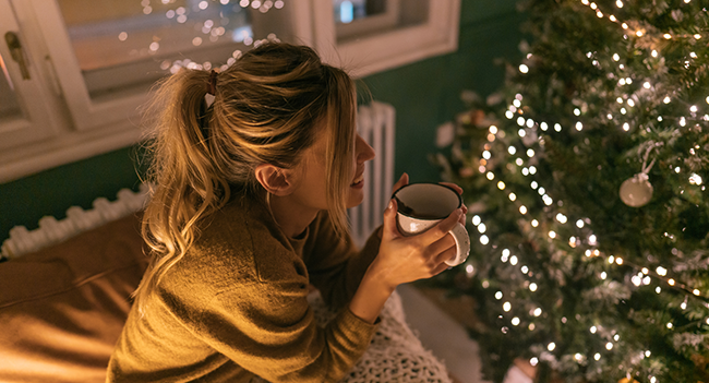 Kvinna med kaffekopp vid julgran